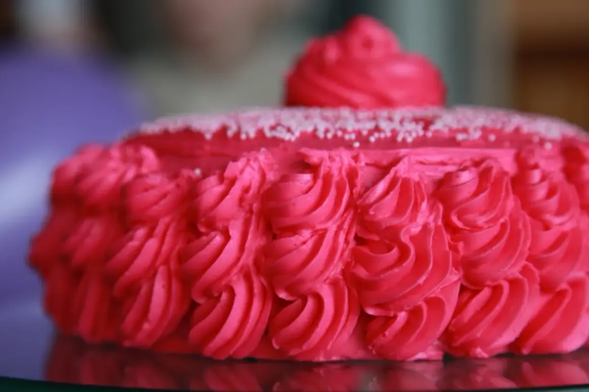 En vacker rosa tårta med rosettmönster i frosting och små vita strössel. Perfekt för ett firande!