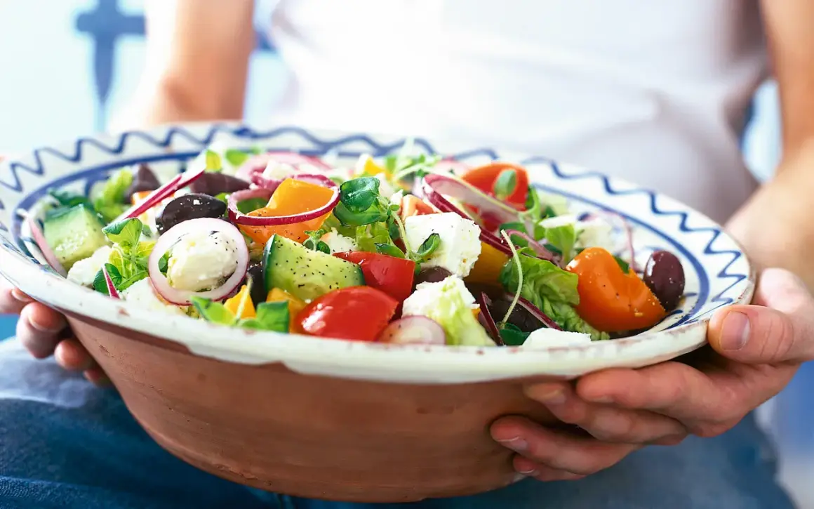 En stor skål med en god sallad till maten, full av färska grönsaker som tomat, gurka, paprika, lök och fetaost.