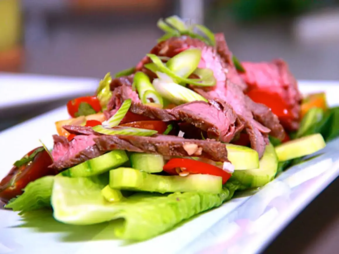 En läcker asiatisk biffsallad med tunt skivad biff, gurka, tomat och salladslök på en bädd av krispig sallad.