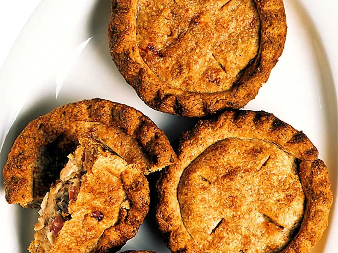 Tre gyllene små pajer på en vit tallrik. En paj är uppskuren och visar ett smakrikt innehåll. Perfekt för en fika!