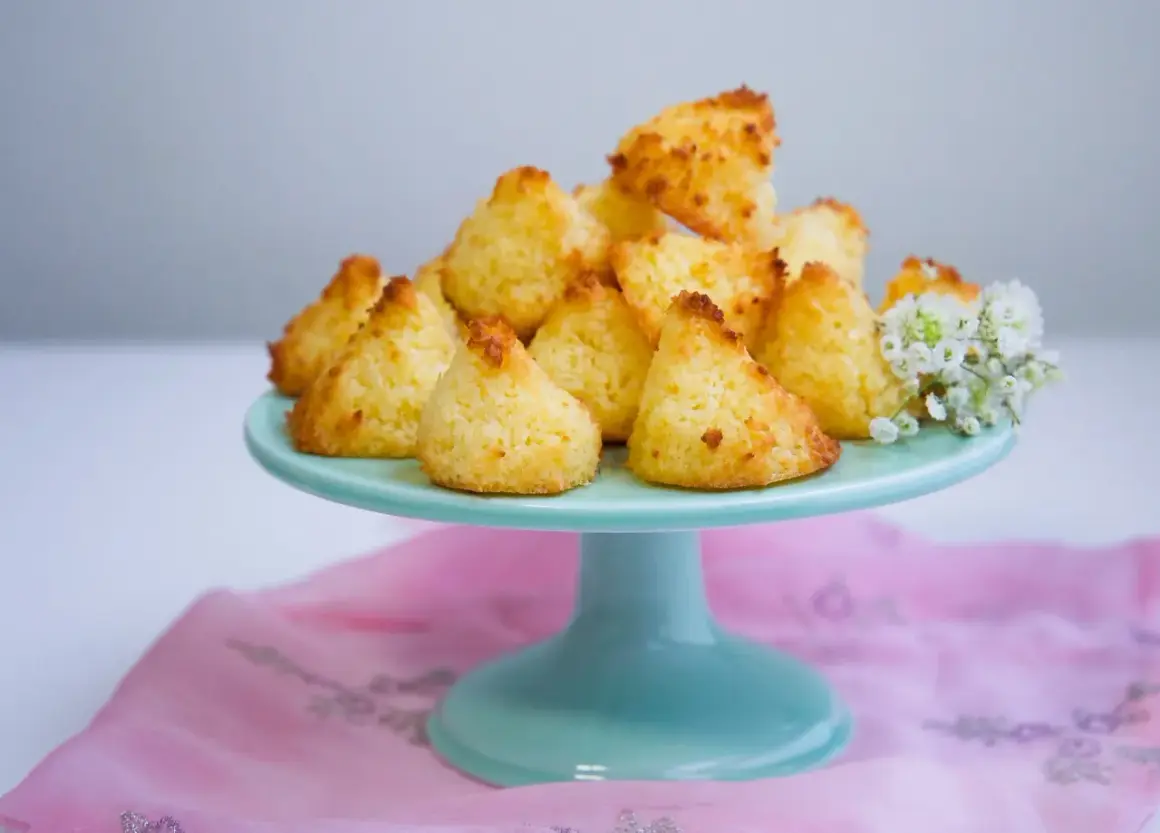 En hög med gyllene kokostoppar på ett turkost fat, redo att avnjutas. Ett enkelt kokostoppar recept som ger ljuvliga små bakverk.