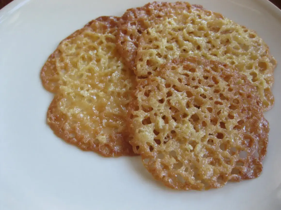 Tre gyllene havreflarn utan sirap ligger på en vit tallrik. De är tunna och krispiga med ett vackert mönster av små hål.