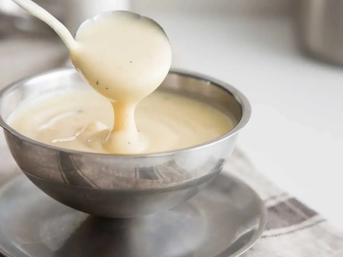 Krämig vaniljsås hälls upp ur en slev i en skål. Perfekt för ditt vaniljsås recept!