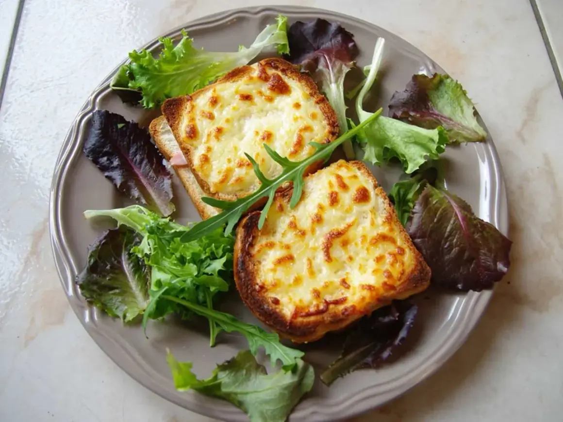 Två gyllene croque monsieur med smält ost och en fräsch sallad på en tallrik.