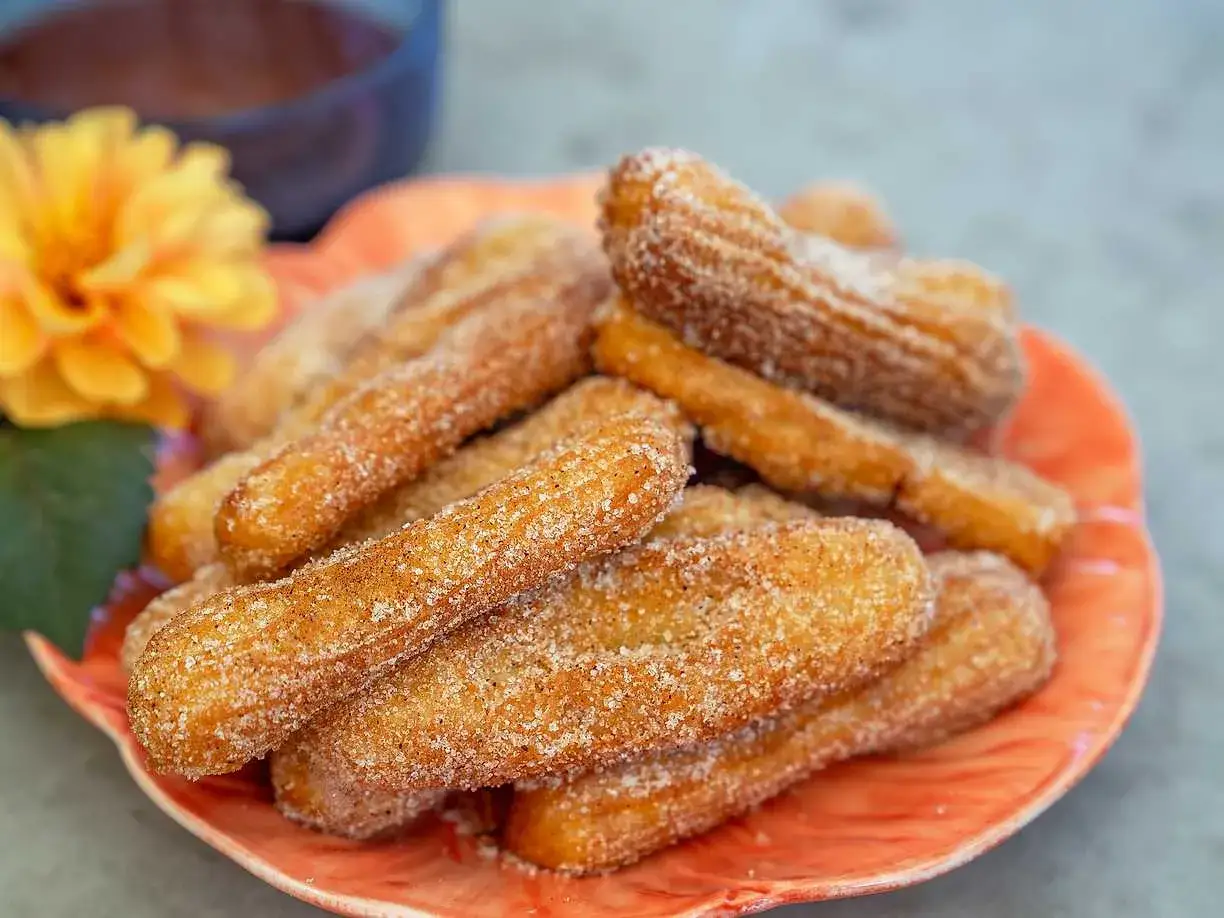 En tallrik med gyllene, socker- och kaneldränkta churros, redo att avnjutas. Ett perfekt churros recept för hemmabruk.