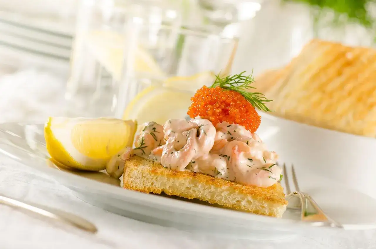 En krämig toast Skagen med räkor, dill och rom, garnerad med en dillkvist och serverad med citronklyfta.
