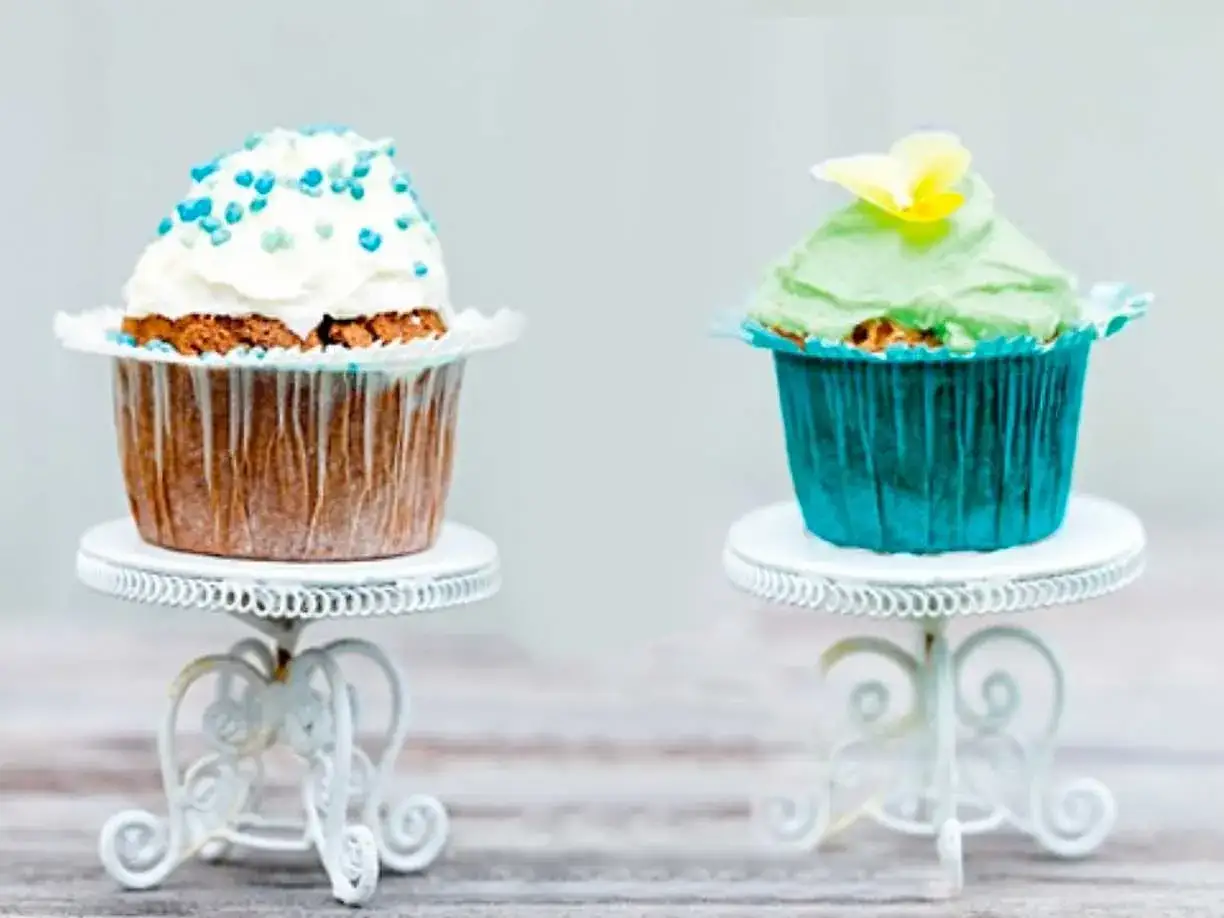 Två glutenfria kladdkakemuffins, en med vit frosting och blå strössel, den andra med grön frosting och en gul blomma.