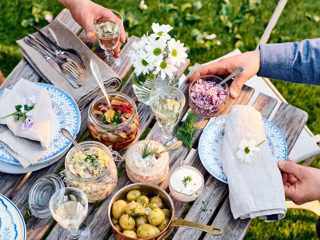 En härlig midsommarmåltid med vegetarisk mat: potatissallad, inlagda grönsaker, sill och färskpotatis. Allt dukat på ett rustikt träbord.