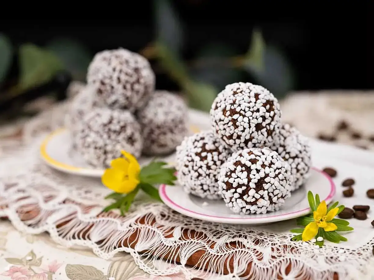 Chokladbollar recept: Mumsiga chokladbollar rullade i pärlsocker, serverade på små fat med gula blommor och kaffebönor.