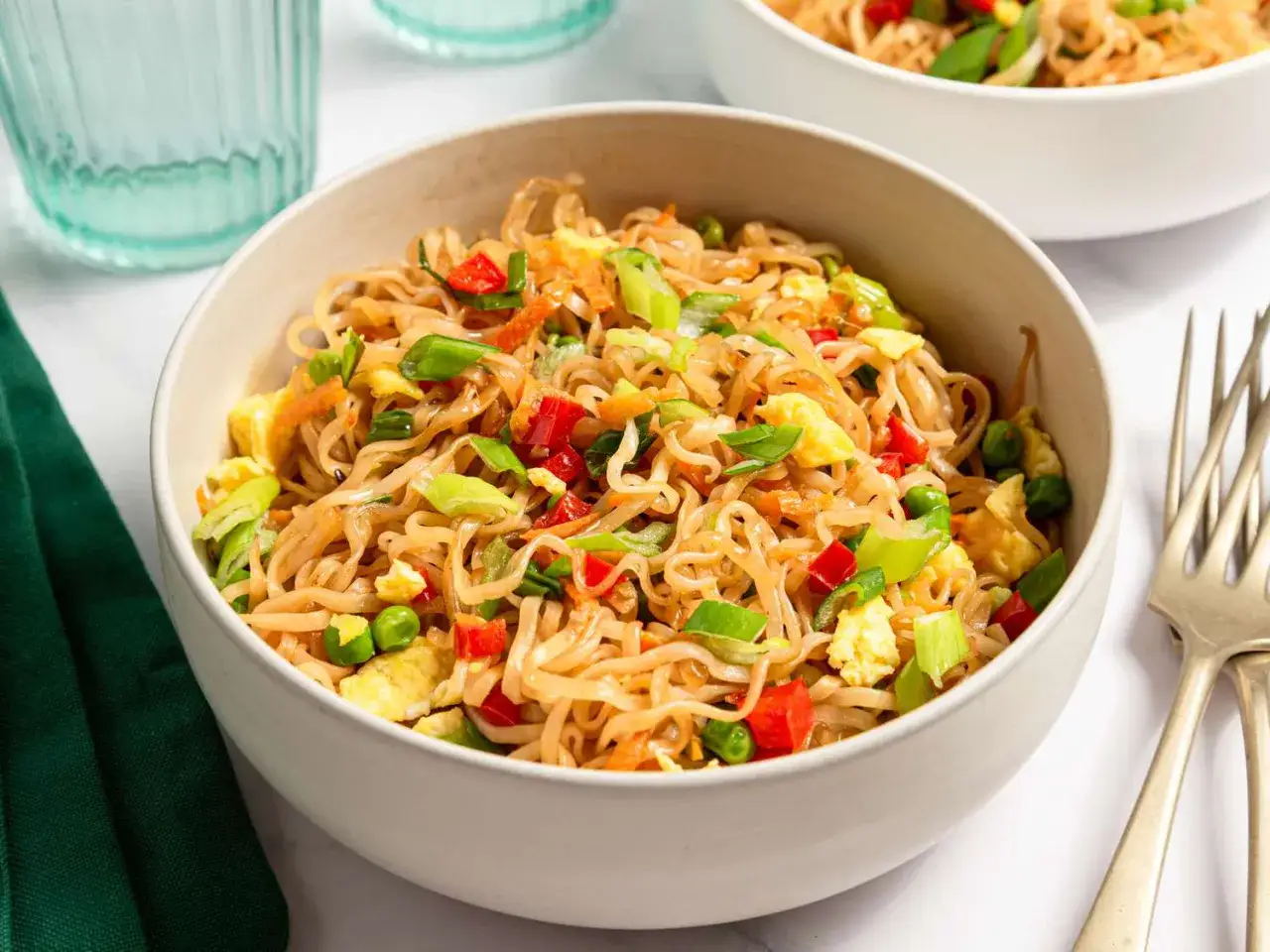 En skål med chow mein med nudlar, ägg, paprika och salladslök.