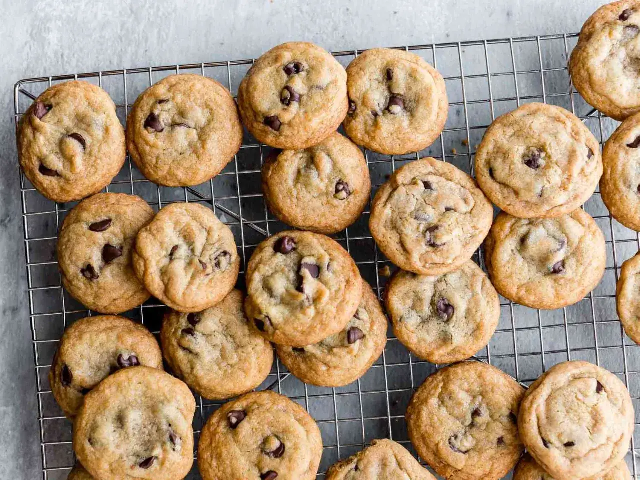 En hög med gyllene, nybakade chocolate chip cookies på ett galler. Perfekt för fikat!