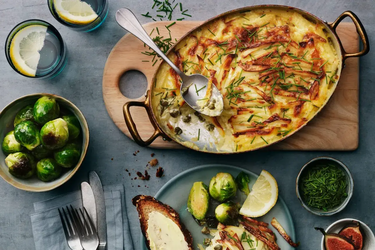 En gyllene vegetarisk Janssons frestelse med krispiga potatisstrimlor och kapris, garnerad med gr&auml;sl&ouml;k. Serveras med brysselk&aring;l och citron.