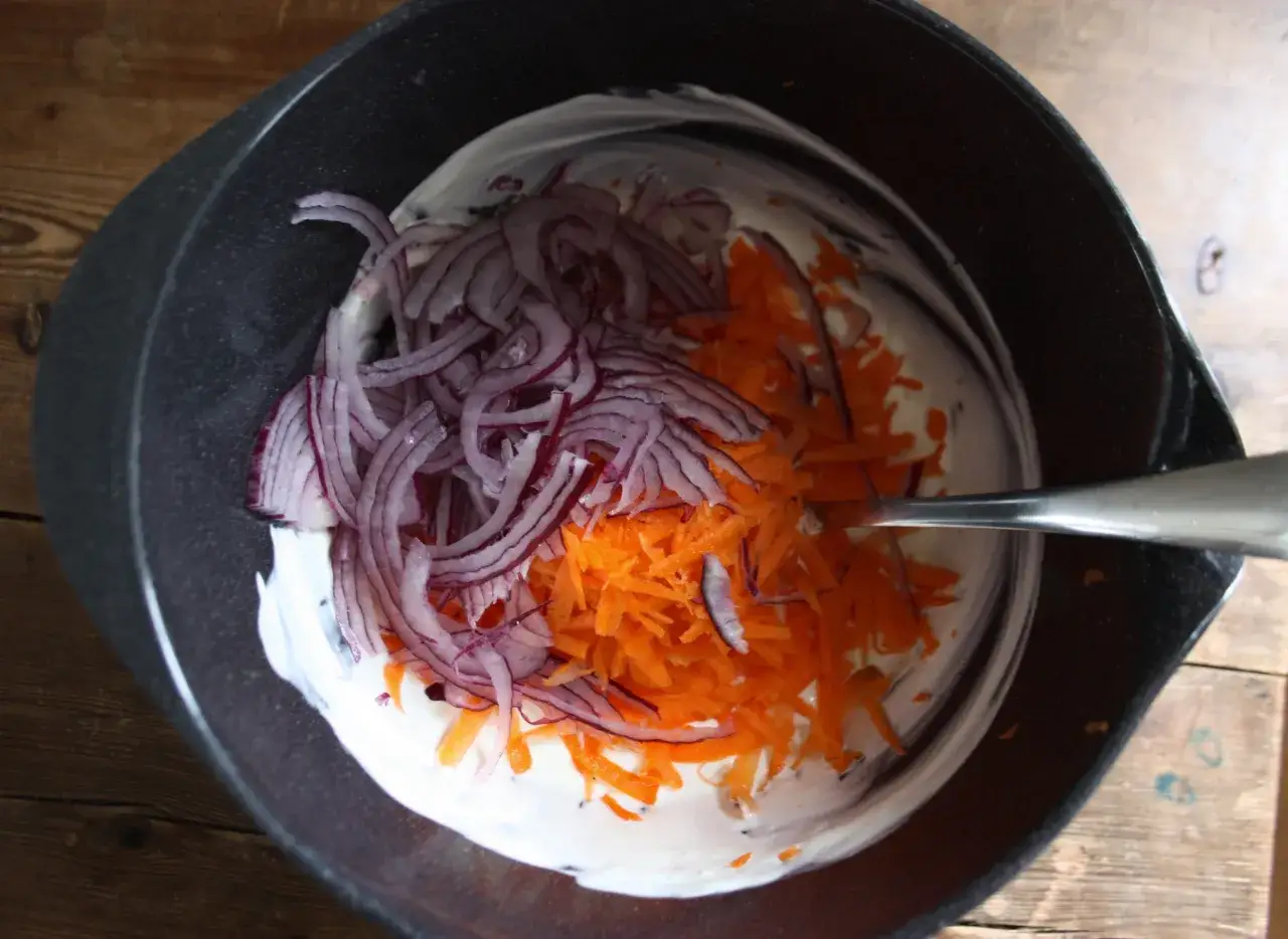 En skål med krämig majonnäs, strimlad morot och rödlök. Ingredienser för godaste coleslaw.