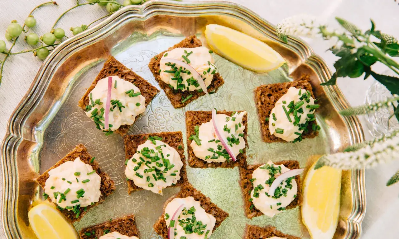 Snittar med lax och philadelphia på mörkt bröd, toppade med gräslök och rödlök. Serveras på ett silverfat med citronklyftor.