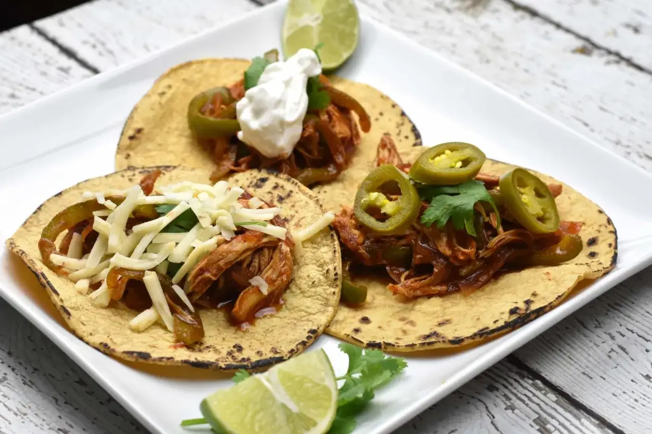 Tre tacos med pulled chicken, jalapeños, ost och gräddfil. Serveras med limeklyftor och koriander.