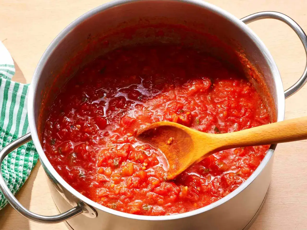 En stor gryta med hemlagad tomatsås, perfekt för ditt nästa tomatsås recept. En träsked rör om i den rika, röda såsen.