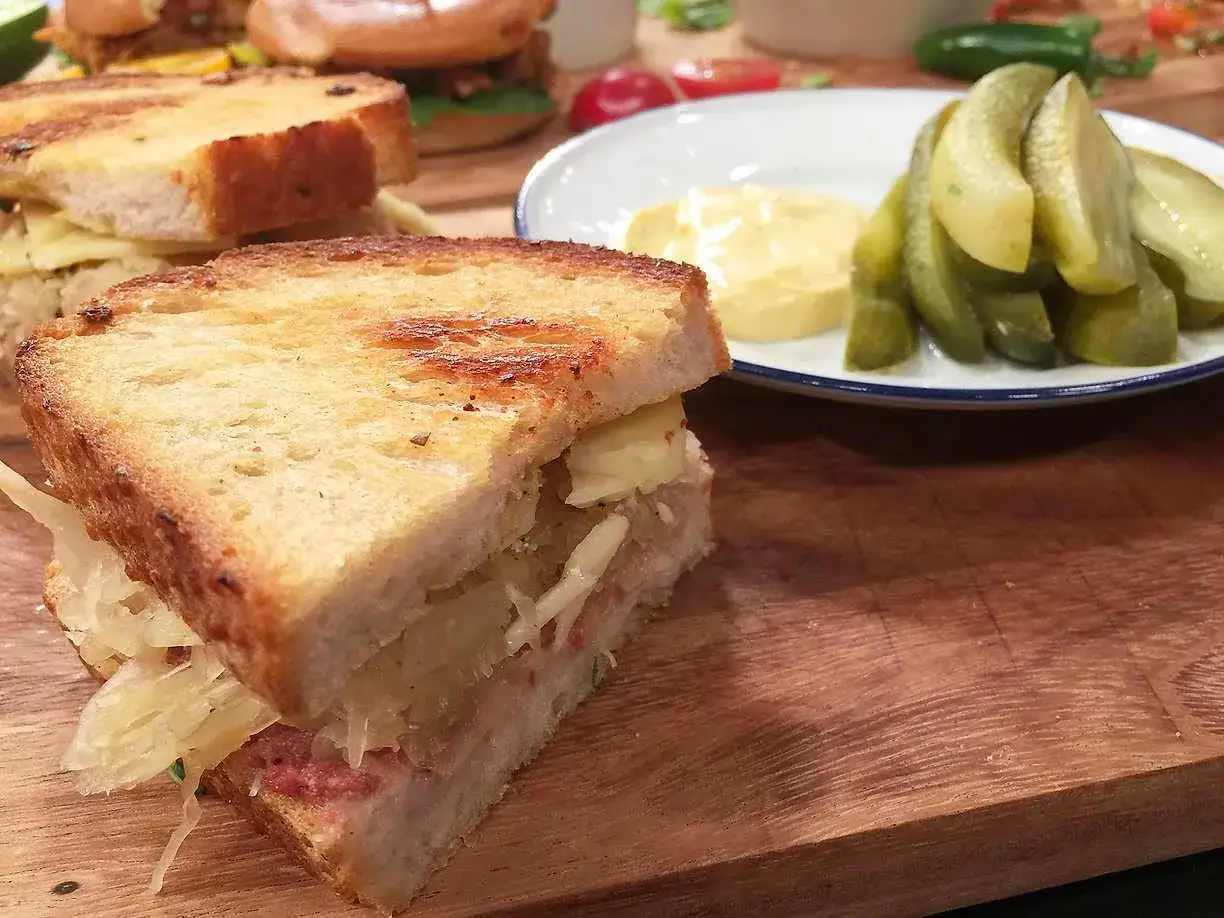 En saftig reuben sandwich med krispigt bröd, syrad kål och ost. Serveras med dillpickles och senap.