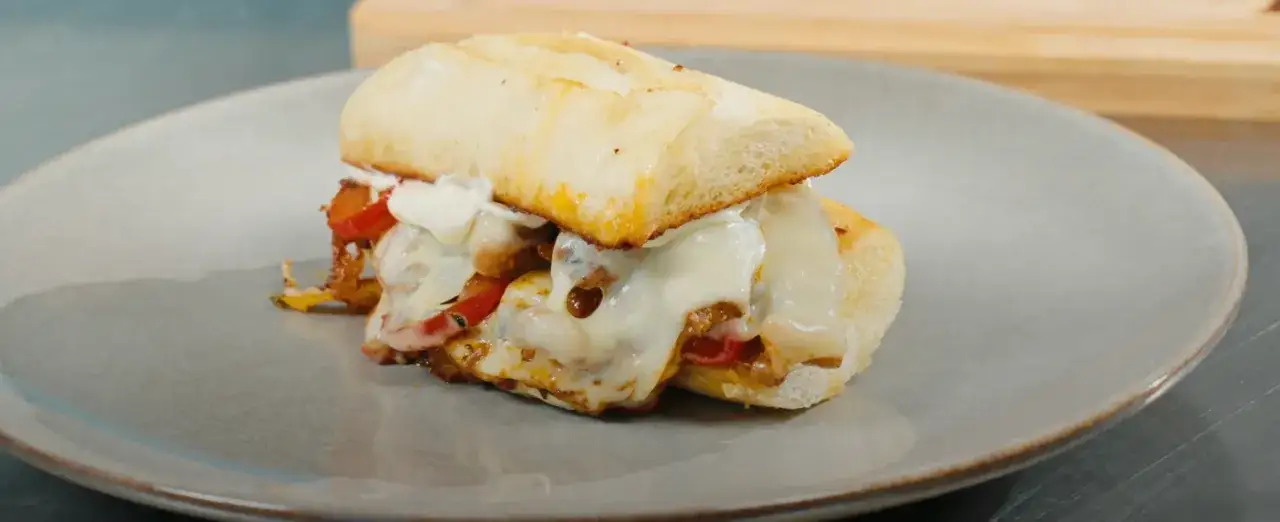 En saftig steak sandwich med smält ost och paprika på en tallrik.