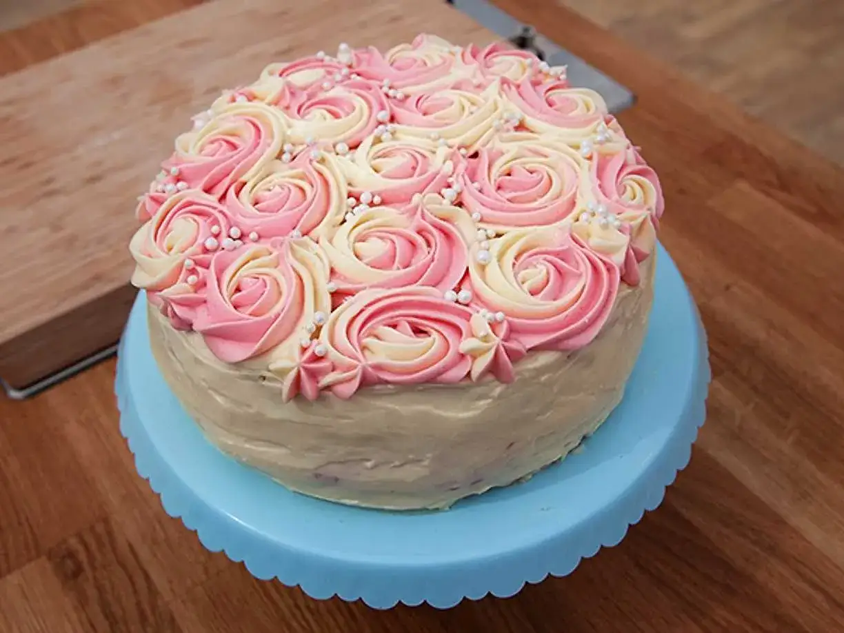 En vacker rosa t&aring;rta med gr&auml;ddrosor i rosa och vitt, dekorerad med sm&aring; p&auml;rlor. Perfekt f&ouml;r ett speciellt tillf&auml;lle!