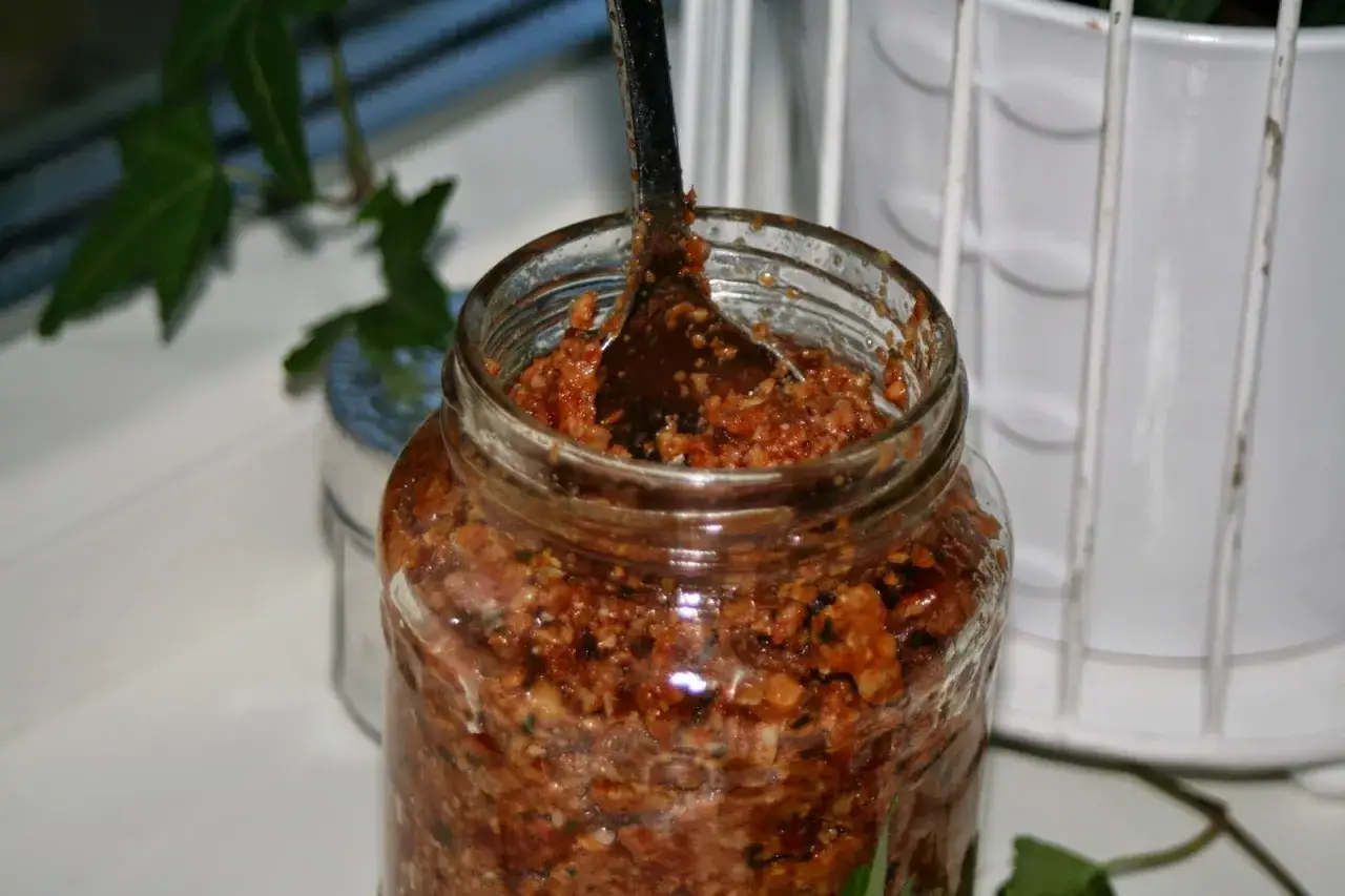 En burk med hemgjord egen pesto, redo att användas. En sked sticker upp ur den smakrika blandningen.