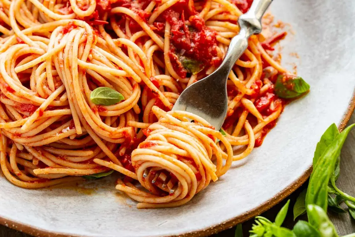 En gaffel snurrar upp en generös portion pasta pomodoro, täckt av en rik tomatsås och garnerad med färsk basilika.