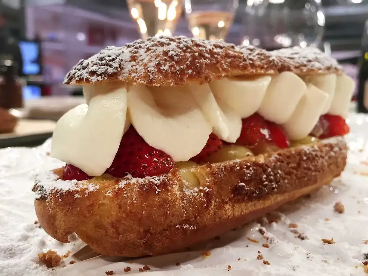 En l&aring;ng, krispig petit choux fylld med vaniljkr&auml;m, f&auml;rska jordgubbar och vispad gr&auml;dde, pudrad med florsocker.