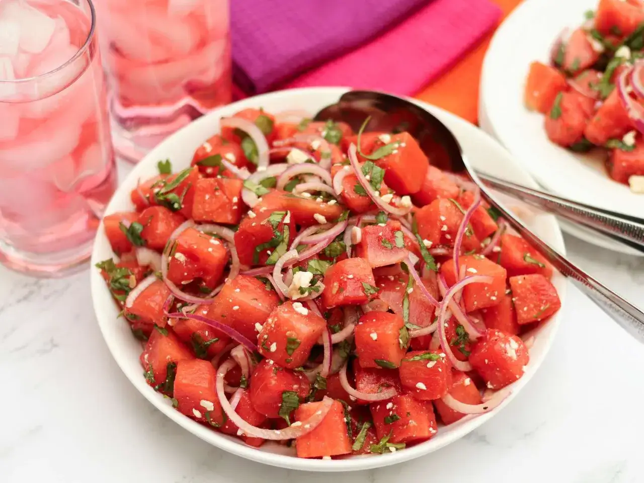 En uppfriskande melon och fetaostsallad med rödlök och mynta, serverad i en vit skål. Perfekt sommarbuffé!