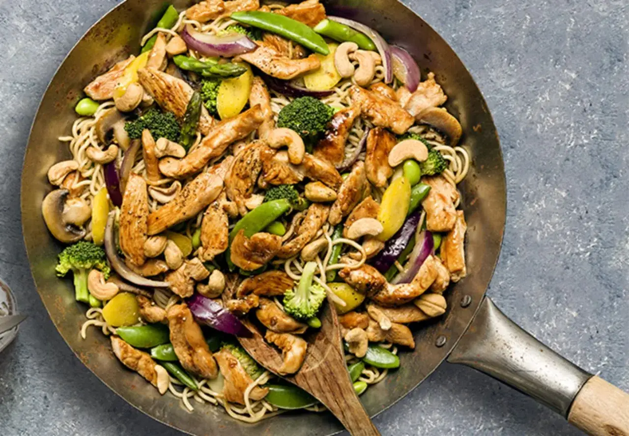 En wok med strimlad kyckling, nudlar, broccoli, sockerärtor, cashewnötter och rödlök. Ett perfekt strimlad kyckling recept för en snabb middag.