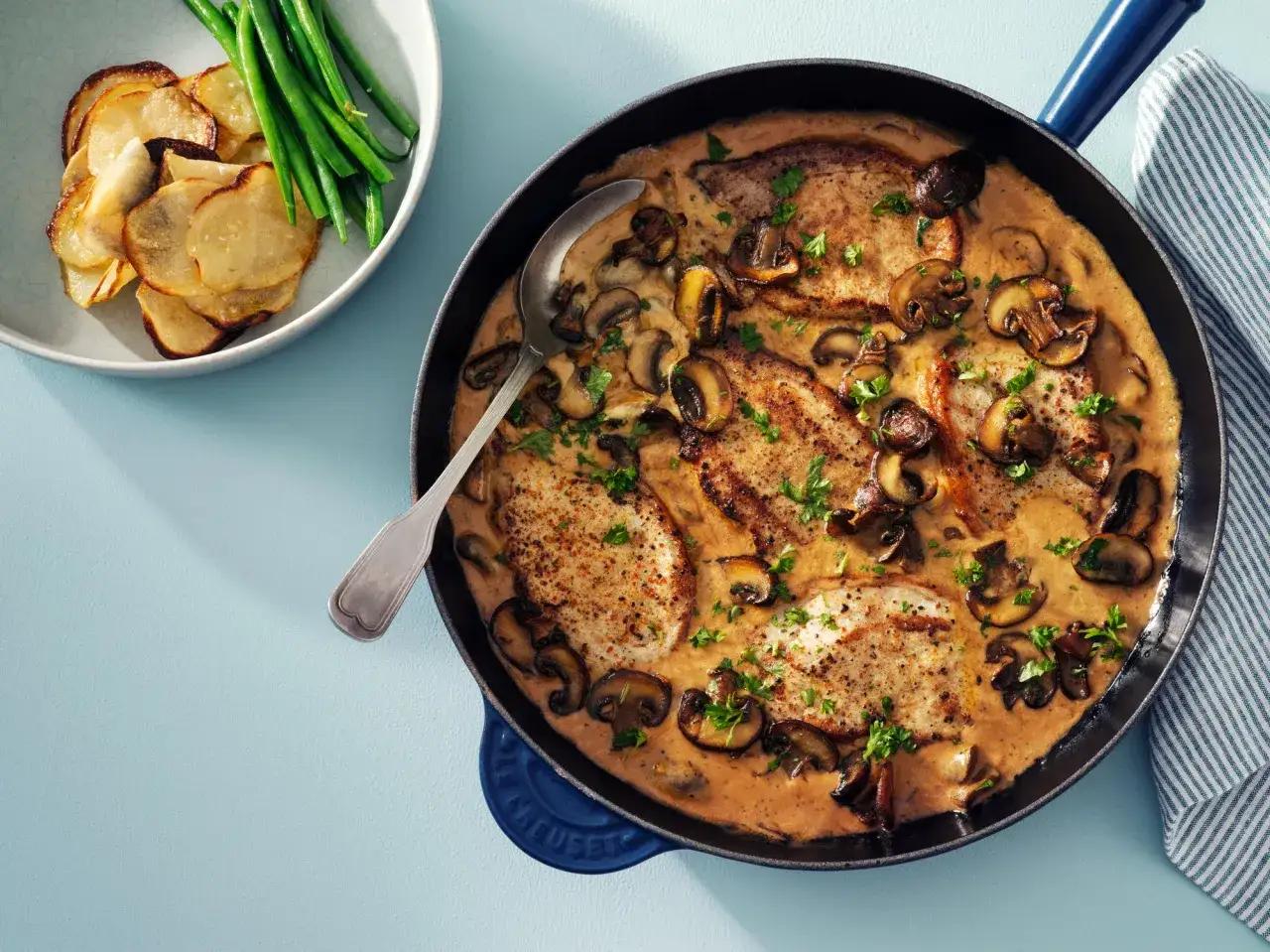 Fläskkotletter i krämig svampsås, serverade med potatischips och gröna bönor. Ett perfekt svampsås recept för middagen.