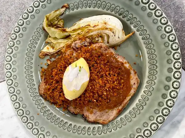 Schnitzel med krispigt täcke och en klick kall sås, garnerad med en blomma. Serveras med ugnsrostad kål.