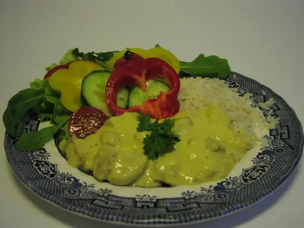 En tallrik med ris, kyckling i krämig currysås, sallad och grönsaker. Ett perfekt currysås recept för en god middag.