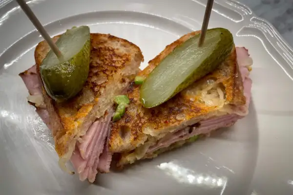 A halved Reuben sandwich with pickles on toothpicks, served on a white plate.