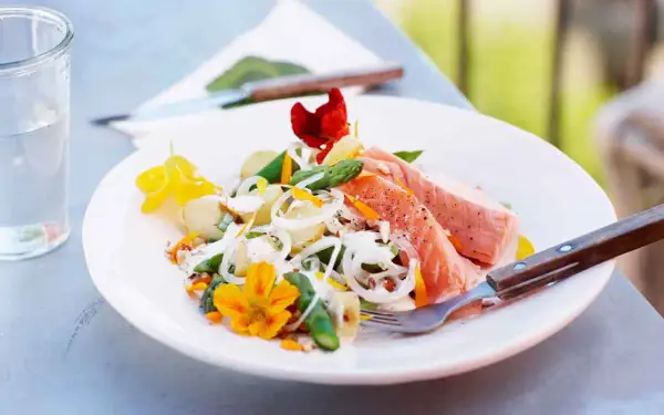 En läcker potatissallad med sparris och lax, dekorerad med ätbara blommor. Perfekt för en somrig lunch utomhus.