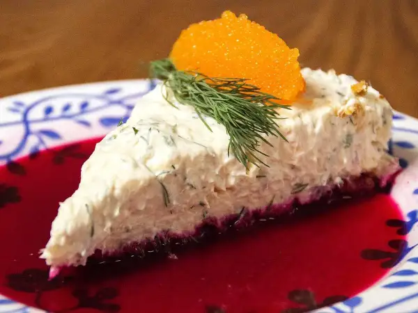 En bit lax cheesecake med dill och rom på en tallrik med rödbetsjuice.